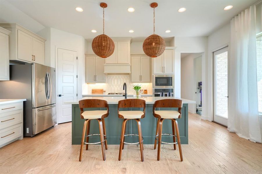 Kitchen featuring a center island with sink, appliances with stainless steel finishes, a breakfast bar, pendant lighting, and light hardwood / wood-style floors