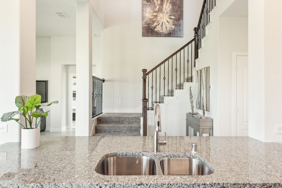 Kitchen island with granite countertop and double sink overlooking open living area with staircase and high ceilings