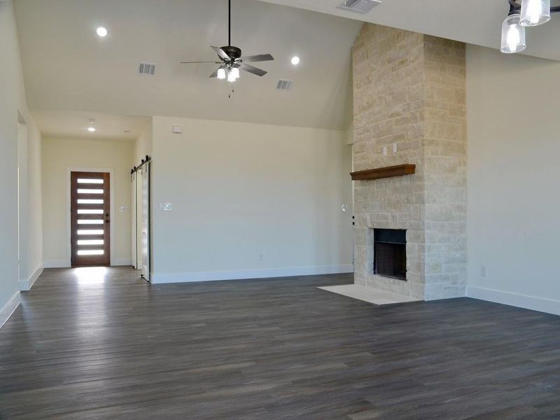 Unfurnished living room with high vaulted ceiling, ceiling fan, dark hardwood / wood-style floors, a barn door, and a fireplace