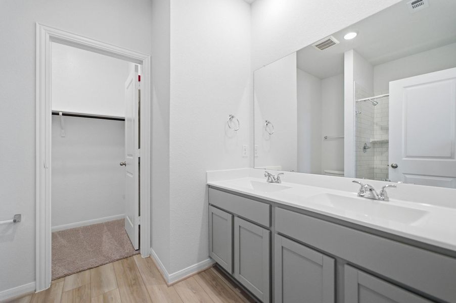 Full bath with double vanity, a shower stall, light wood-style flooring, and a walk in closet