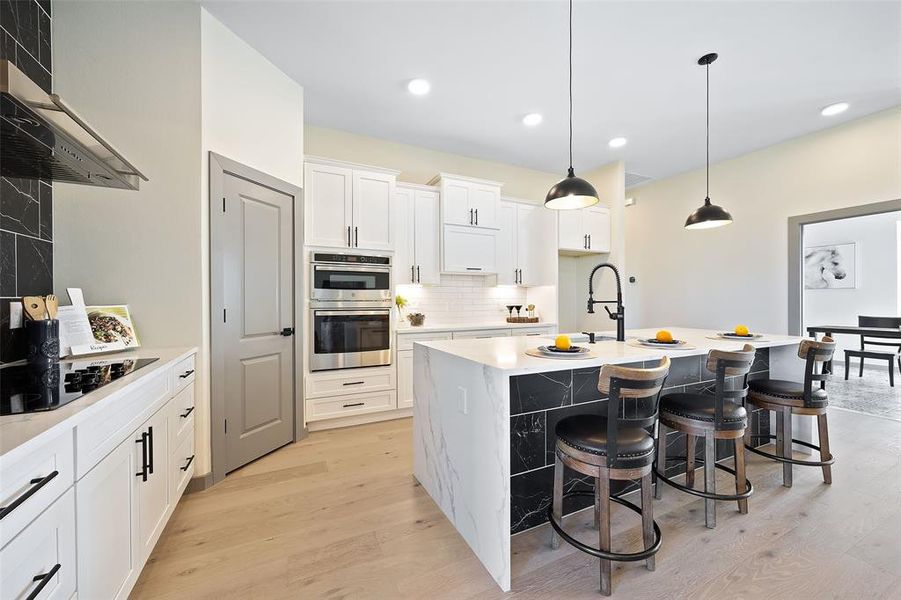 Kitchen with range hood, light hardwood / wood-style flooring, stainless steel double oven, and a kitchen island with sink