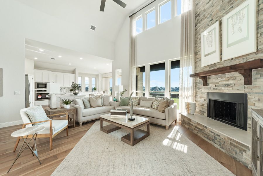 Open-concept living room with vaulted ceiling, stone fireplace, and hardwood floors open to kitchen