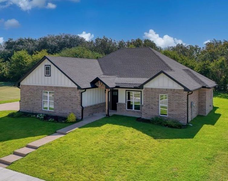 View of front of property with board and batten siding, a front yard, brick siding, and roof with shingles View of front of property with board and batten siding, a front yard, brick siding, and roof with shingles