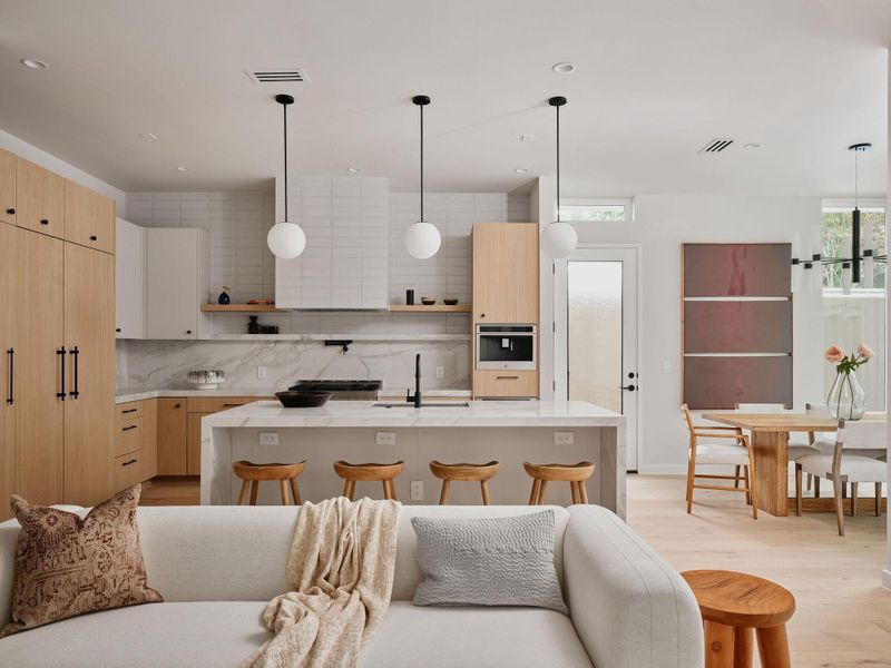 Open-concept kitchen featuring an oversized island with seating, integrated appliances, and light wood-finish cabinetry