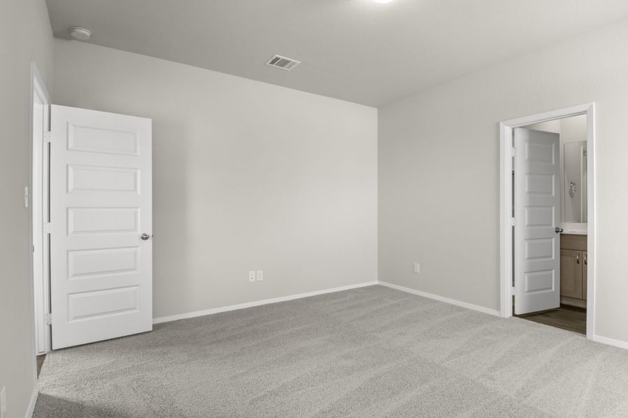 Image of primary bedroom with tan carpet and light grey walls and a white door