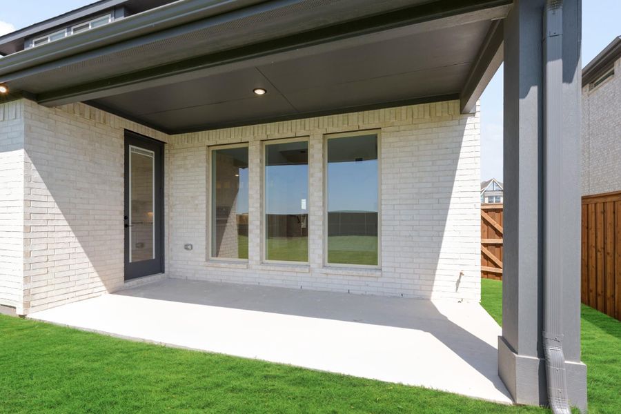Covered back patio with concrete floor, white brick exterior, large windows, and green lawn