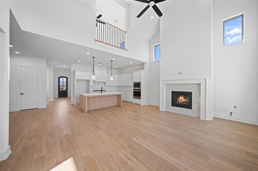 Unfurnished living room with high vaulted ceiling, a glass covered fireplace, recessed lighting, light wood-style floors, and a ceiling fan