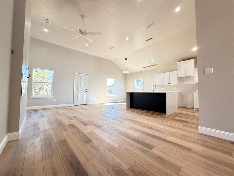 Unfurnished living room with light wood-style floors, ceiling fan, recessed lighting, high vaulted ceiling, and a textured ceiling Unfurnished living room with light wood-style floors, ceiling fan, recessed lighting, high vaulted ceiling, and a textured ceiling
