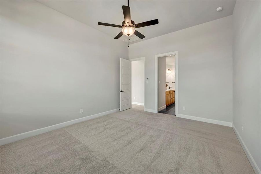 Unfurnished bedroom with light colored carpet, ceiling fan, and connected bathroom