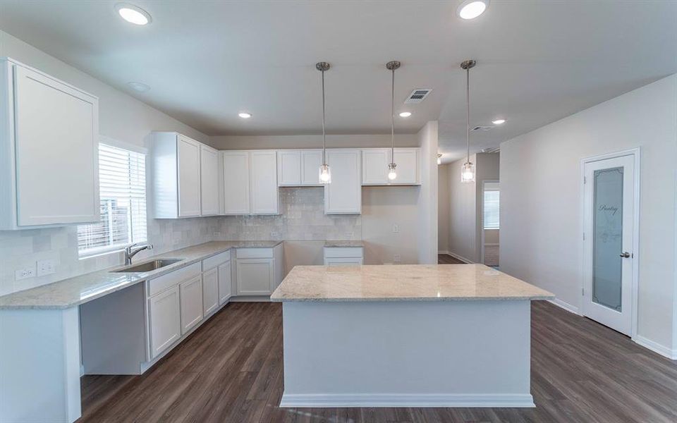 Kitchen featuring an expansive island with a light-toned countertop, white cabinetry, a tiled backsplash, and wood-finish flooring