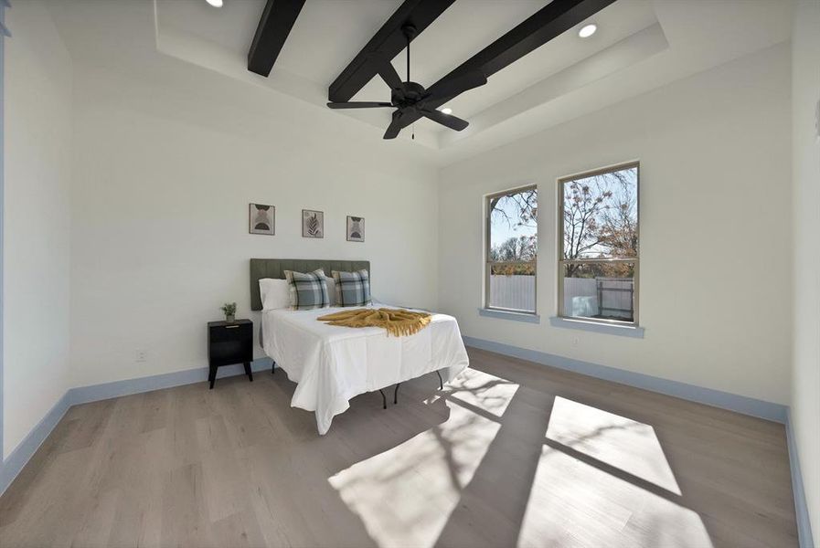 Bedroom featuring beamed ceiling, light wood-type flooring, a ceiling fan, a raised ceiling, and recessed lighting