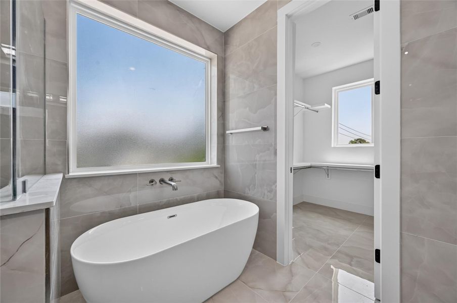 Relaxing soaking tub sits under a large frosted window that boasts immense natural light