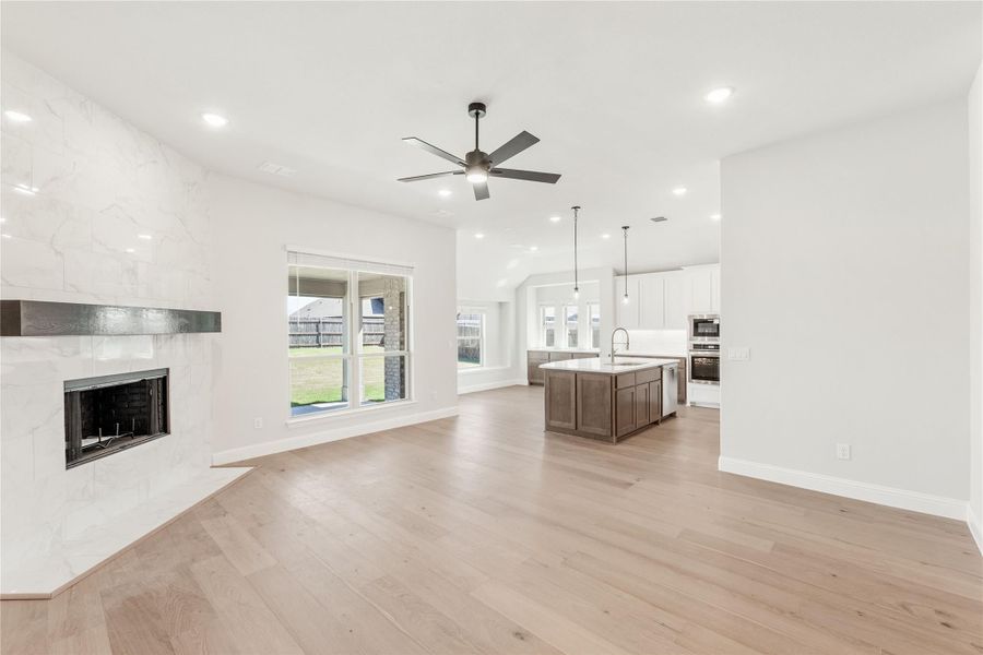 Open living area with tile fireplace, hardwood floors, and open-concept kitchen with island in background