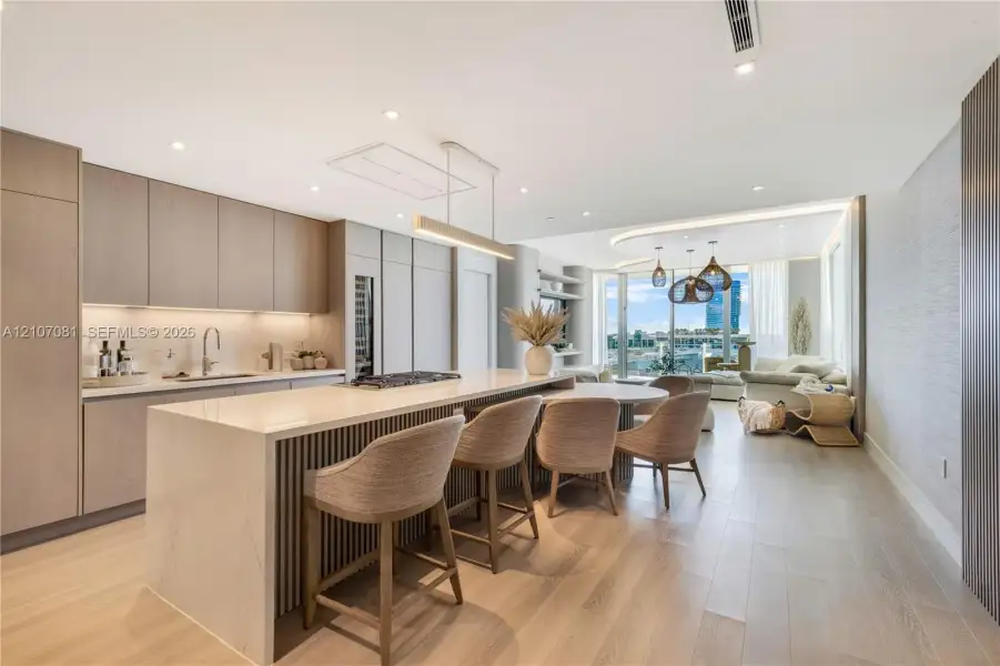 Kitchen featuring floor-to-ceiling cabinetry, a waterfall-edge island, wood-finish flooring, integrated wine refrigeration, and recessed lighting Kitchen featuring floor-to-ceiling cabinetry, a waterfall-edge island, wood-finish flooring, integrated wine refrigeration, and recessed lighting