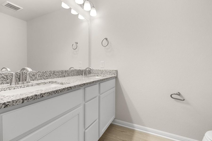 The property features a vanity with a granite countertop, dual sinks with chrome faucets, and white cabinetry