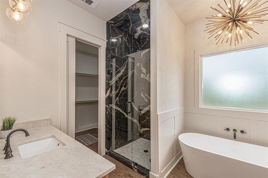 Full bath with vanity, a marble finish shower, a soaking tub, a spacious closet, and light wood finished floors