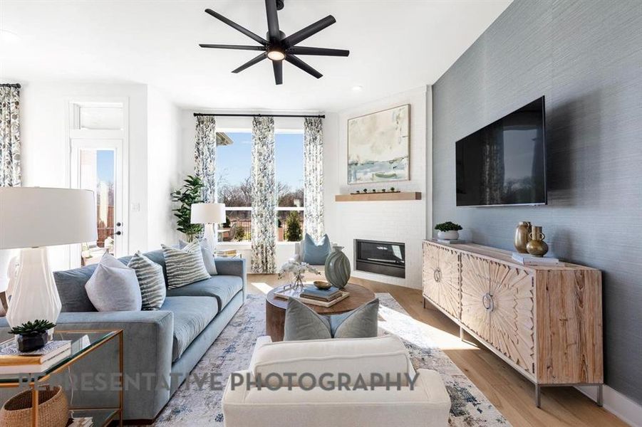 Living area with a glass covered fireplace, wood finished floors, and ceiling fan