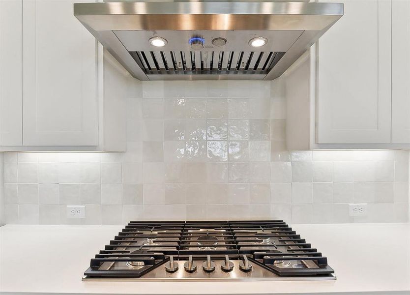 The kitchen features a stainless steel range hood with integrated lighting, a gas cooktop, and a white tiled backsplash