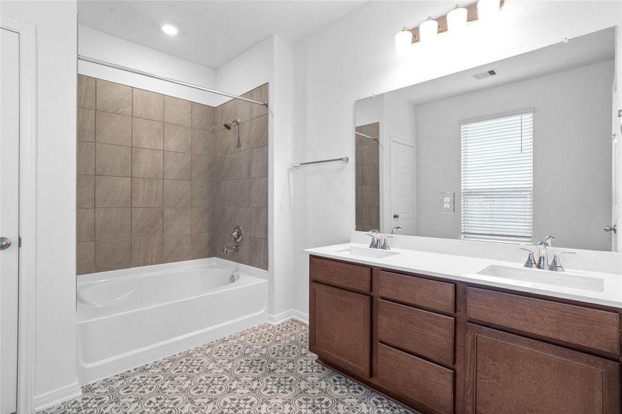 This beautiful primary bathroom is move-in ready! It showcases stained cabinetry paired with light countertops, dual vanity sinks, a large mirror, high ceilings, custom paint, gorgeous decorative tile flooring, tub/shower combination, and stylish modern finishes throughout.