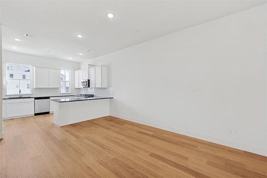 Kitchen featuring white cabinets, light wood-type flooring, appliances with stainless steel finishes, and tasteful backsplash Kitchen featuring white cabinets, light wood-type flooring, appliances with stainless steel finishes, and tasteful backsplash
