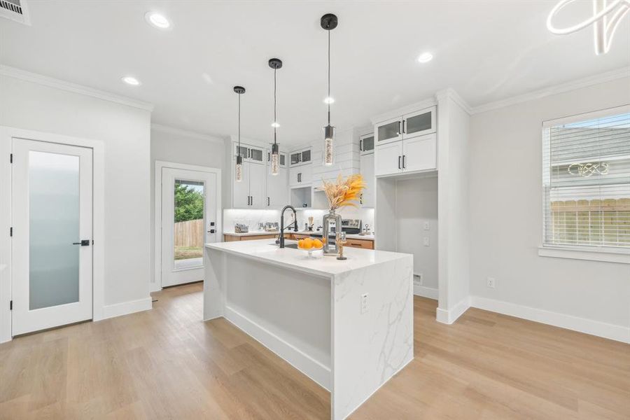 Kitchen featuring backsplash, light wood-type flooring, decorative light fixtures, white cabinetry, and a center island with sink