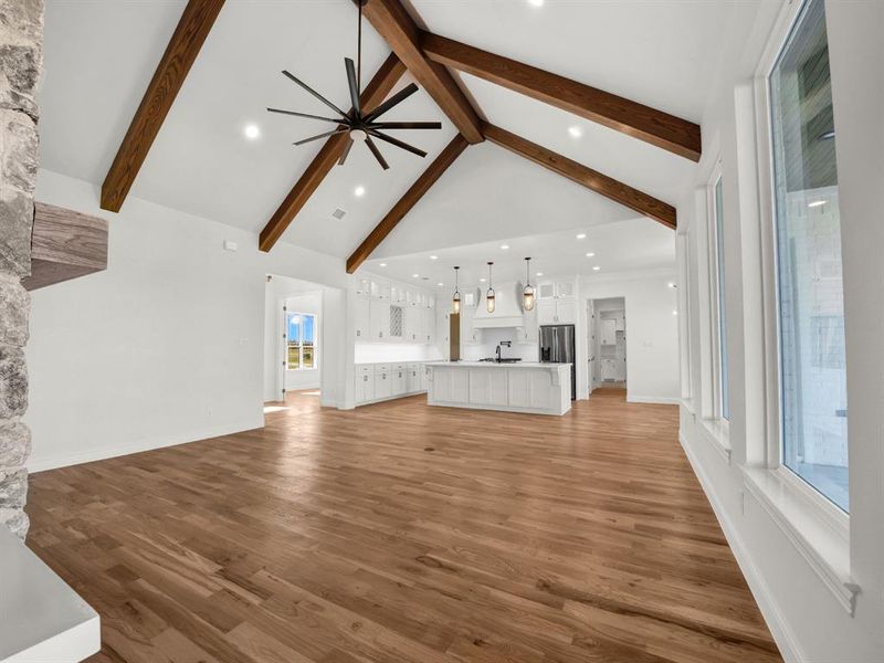 Unfurnished living room with beam ceiling, light hardwood / wood-style flooring, ceiling fan, and a healthy amount of sunlight