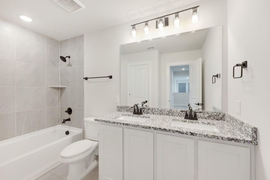 Bathroom with double sink vanity, granite countertop, white cabinets, tub-shower combo, and large mirror with light bar