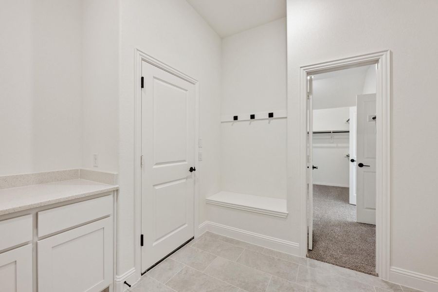 Mudroom with built-in bench, wall hooks, white cabinets, and doorway leading to a walk-in closet Mudroom with built-in bench, wall hooks, white cabinets, and doorway leading to a walk-in closet