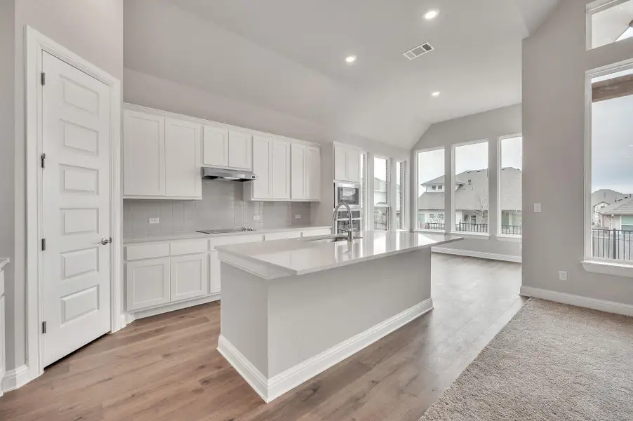 Kitchen featuring under cabinet range hood, white cabinetry, and light countertops Kitchen featuring under cabinet range hood, white cabinetry, and light countertops