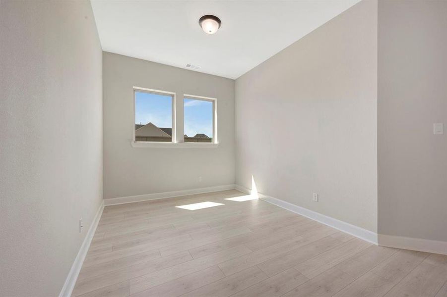 Room featuring light wood-finish flooring, neutral wall paint, white baseboards, and two window openings