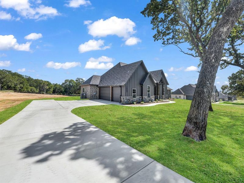Modern inspired farmhouse featuring stone siding, driveway, board and batten siding, and a front lawn