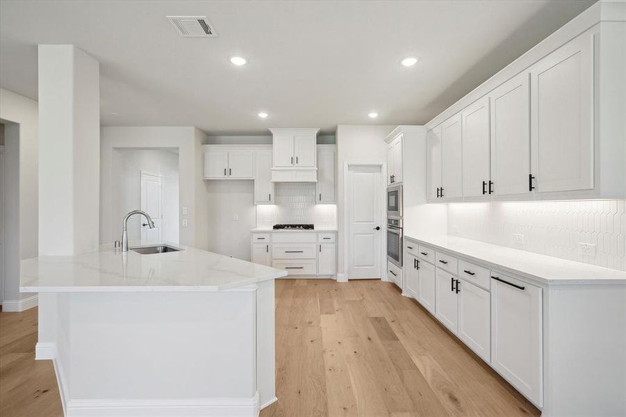 Kitchen featuring a sink, decorative backsplash, light wood finished floors, white cabinetry, and recessed lighting