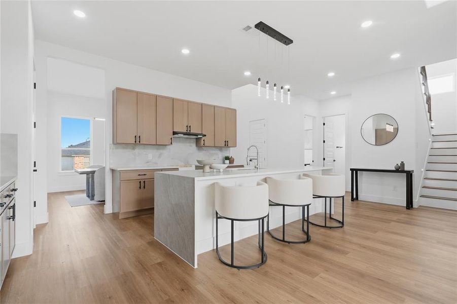 Kitchen featuring a breakfast bar, healthy amount of natural light, a kitchen island with sink, and decorative light fixtures