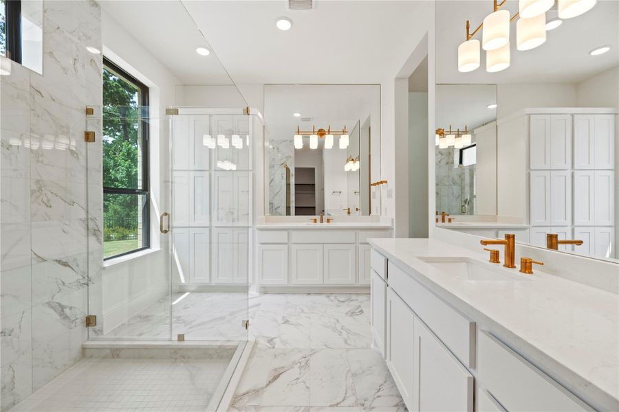 Enjoy the spa-like luxury in this stunning primary bathroom, featuring dual vanities with quartz countertops, gold fixtures, and an oversized glass-enclosed shower.
