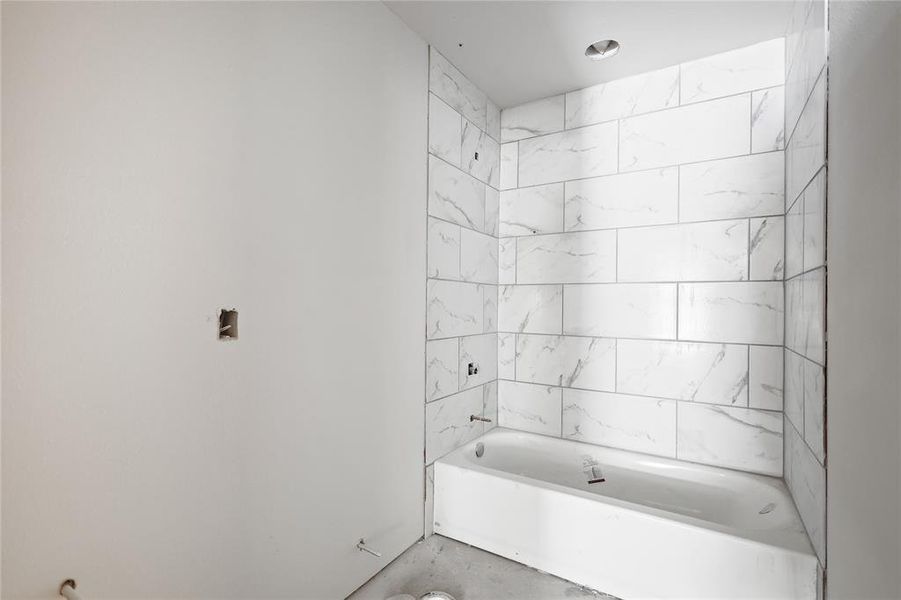 Bathroom featuring a white bathtub and white tile surround with grey veining