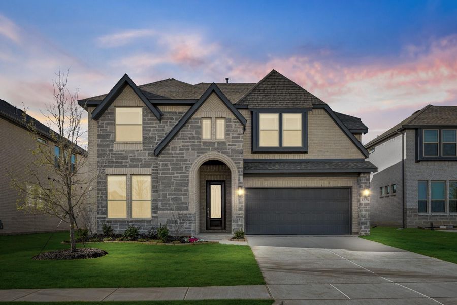 Two-story home with stone exterior, arched entry, two-car garage, and manicured front lawn at dusk Two-story home with stone exterior, arched entry, two-car garage, and manicured front lawn at dusk