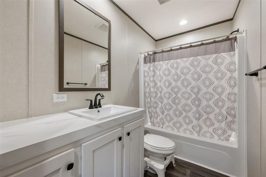 Bathroom with shower / bathtub combination with curtain, vanity, ornamental molding, dark wood finished floors, and a decorative wall
