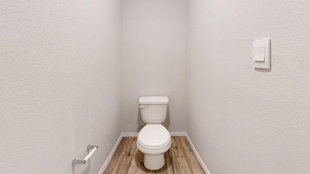 Private water closet featuring a standard white toilet, wood-finish flooring, and light-toned textured walls Private water closet featuring a standard white toilet, wood-finish flooring, and light-toned textured walls