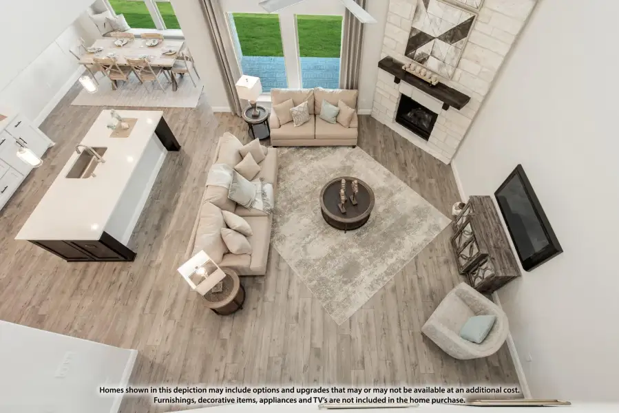 Open-concept living area with stone fireplace, sectional sofa, and wood floors, viewed from above with kitchen and dining area visible.