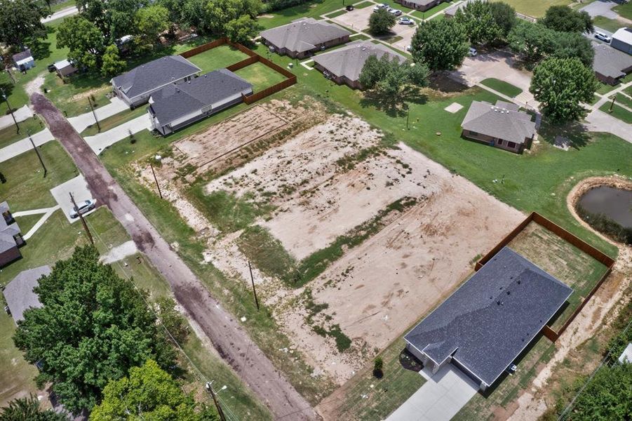 Expansive cleared land parcel with defined property boundaries, bordered by a paved road and established residences