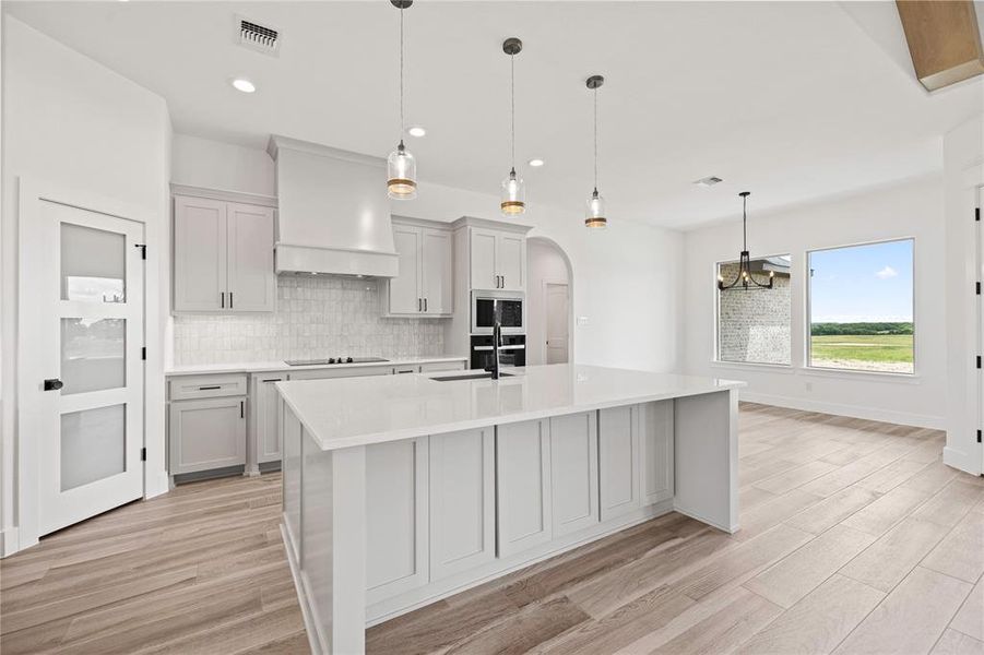 Kitchen featuring tasteful backsplash, hanging light fixtures, light wood-style floors, light stone counters, and recessed lighting Kitchen featuring tasteful backsplash, hanging light fixtures, light wood-style floors, light stone counters, and recessed lighting