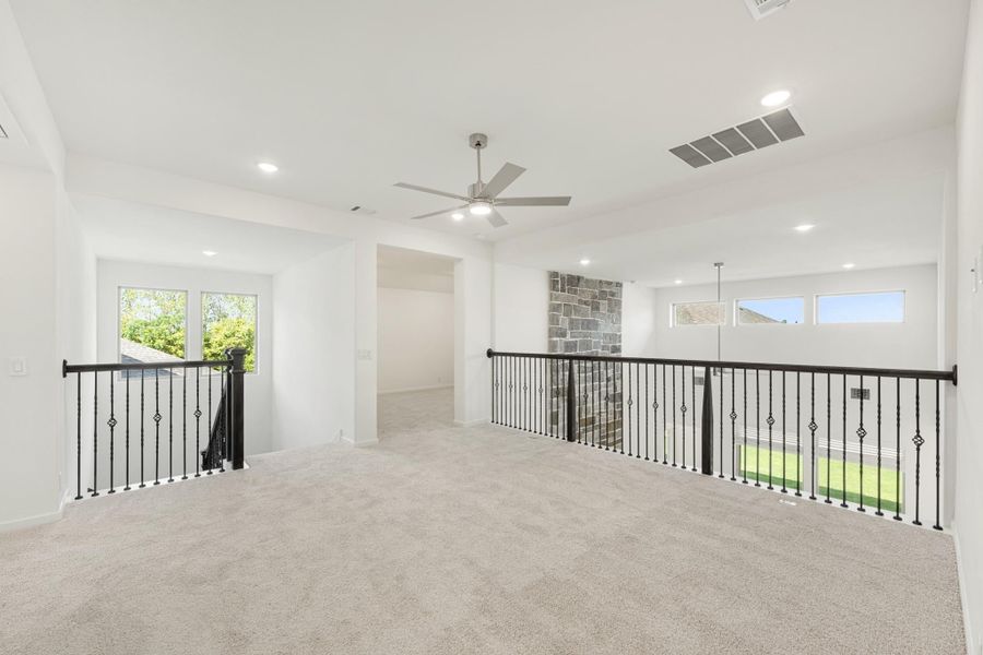Open upstairs loft with carpet, ceiling fan, and black iron stair railing overlooking lower level