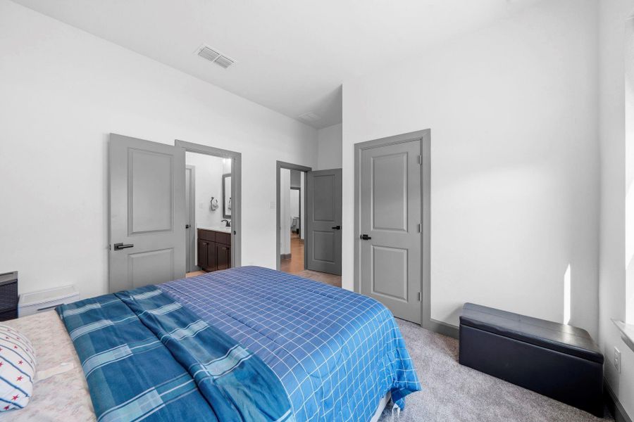 Spacious bedroom featuring high ceilings, soft carpeting, and convenient access to a nearby bathroom.