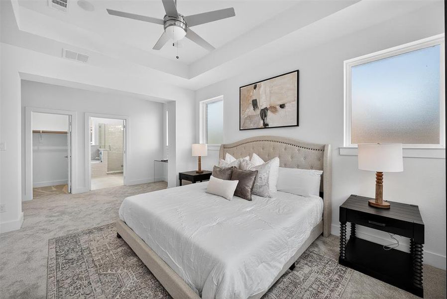 Bedroom featuring carpet floors, a spacious closet, a raised ceiling, ceiling fan, and ensuite bath