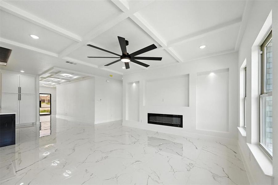 Unfurnished living room featuring recessed lighting, light marble finish floors, a glass covered fireplace, beam ceiling, and coffered ceiling