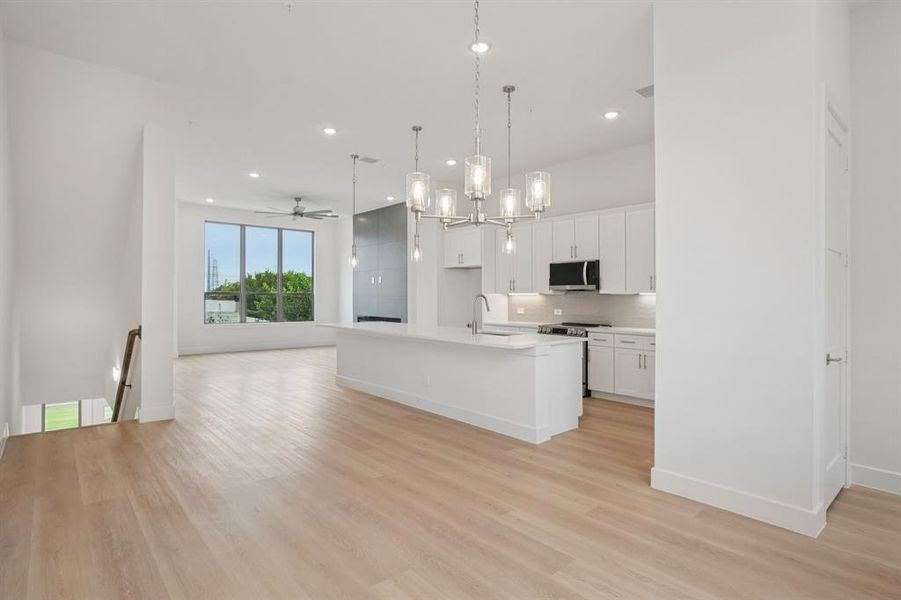 Kitchen featuring open floor plan, a chandelier, a center island with sink, white cabinetry, and appliances with stainless steel finishes