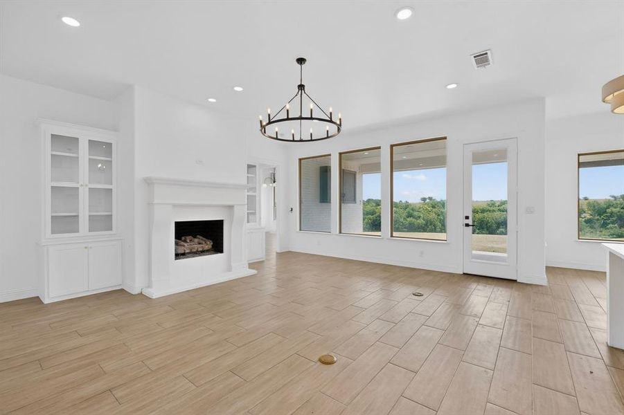 Spacious living area featuring a central fireplace with mantle, built-in display cabinetry, wood-finish flooring, and multiple large windows showcasing outdoor scenery Spacious living area featuring a central fireplace with mantle, built-in display cabinetry, wood-finish flooring, and multiple large windows showcasing outdoor scenery