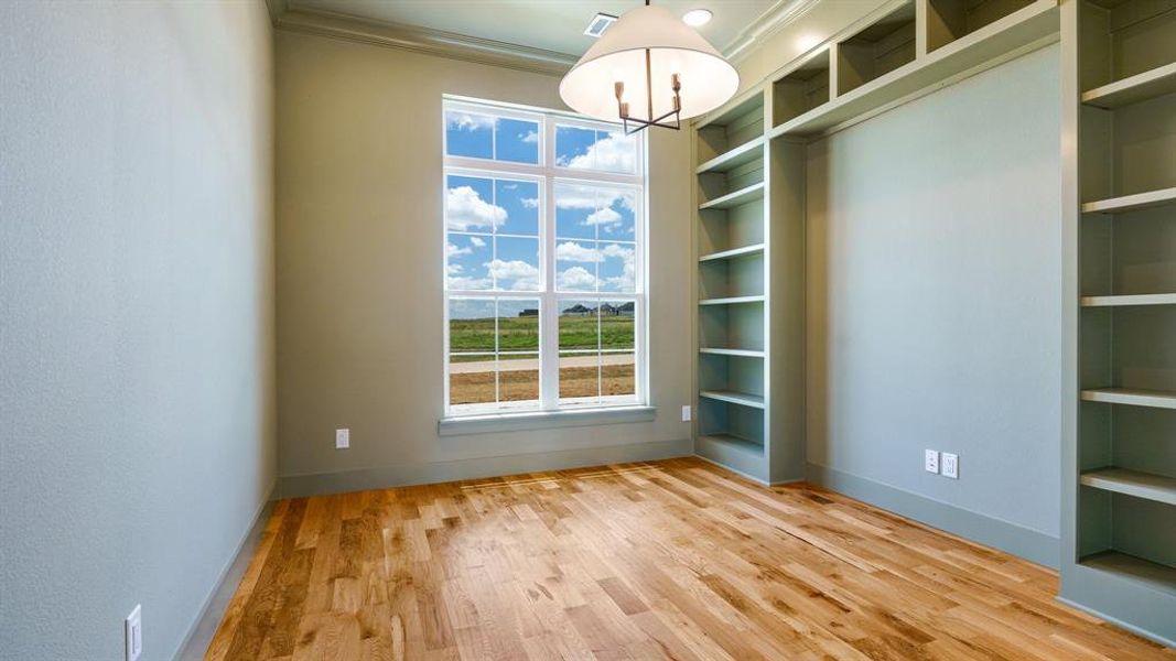 Unfurnished room with built in shelves, a chandelier, light hardwood / wood-style flooring, and crown molding