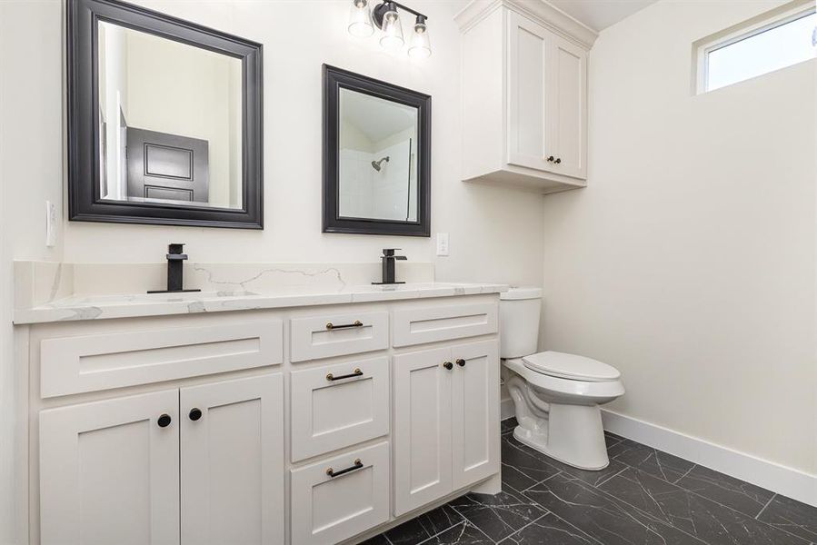 Bathroom featuring baseboards, toilet, double vanity, marble finish floor, and a sink