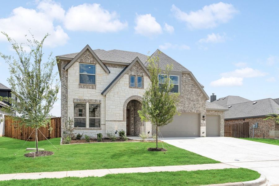 Two-story home with stone and brick exterior, arched entry, two-car garage, and manicured front lawn